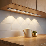 Barra LED instalada bajo un armario de cocina real, encendida iluminando la encimera
