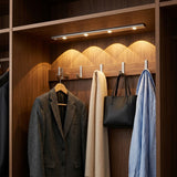 Barra LED instalada dentro de un closet iluminando ropa colgada, uso real