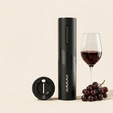 Destapador sacacorchos eléctrico junto a copa de vino y uvas